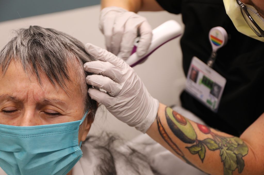 Patient Jean Henderson has her hair shaved by RN Peg Torelli Wauters. Henderson had high-frequency ultrasound brain surgery led by OHSU neurosurgeon Ahmed Raslan and his team on Wednesday, March 30, 2022. Jean Henderson is the first patient to undergo this treatment in Oregon. She has had a tremor for four years, which limited her abilities to care for herself, and this surgery corrected that tremor in her right hand/arm in just a few hours with no incision. (OHSU/Christine Torres Hicks)