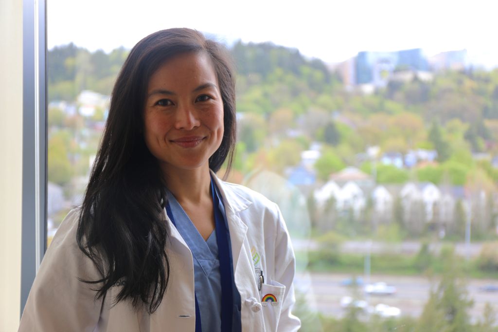 Geolani Dy, M.D. poses by a window with OHSU Marquam Hill in the background.