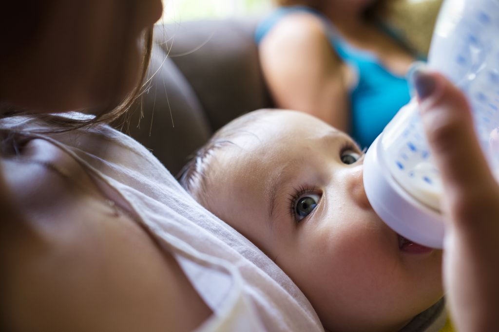 Closeup of infant's face, being held and fed from a bottle