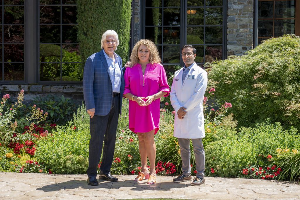 Dale and Julie Burghardt stand with Shyam Joshi, M.D., outside the Burghardt's home on a sunny day.