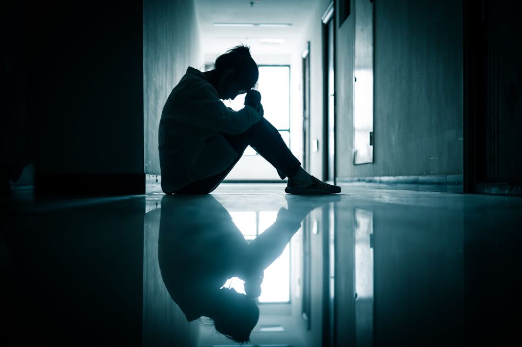 Silhouette of a sad woman sitting in a hallway.
