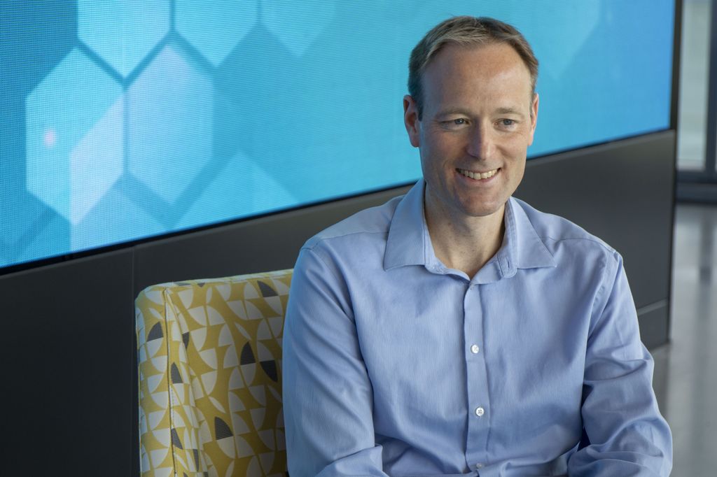Portrait of Jeff Tyner, Ph.D., a balding, white male in a blue collared shirt, sitting in front of a bright turquoise wall.