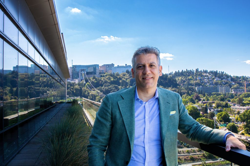 Steven Mansoor, M.D., Ph.D. stands atop a terrace at the OHSU Center for Health & Healing with a view of OHSU Marquam Hill in the background.