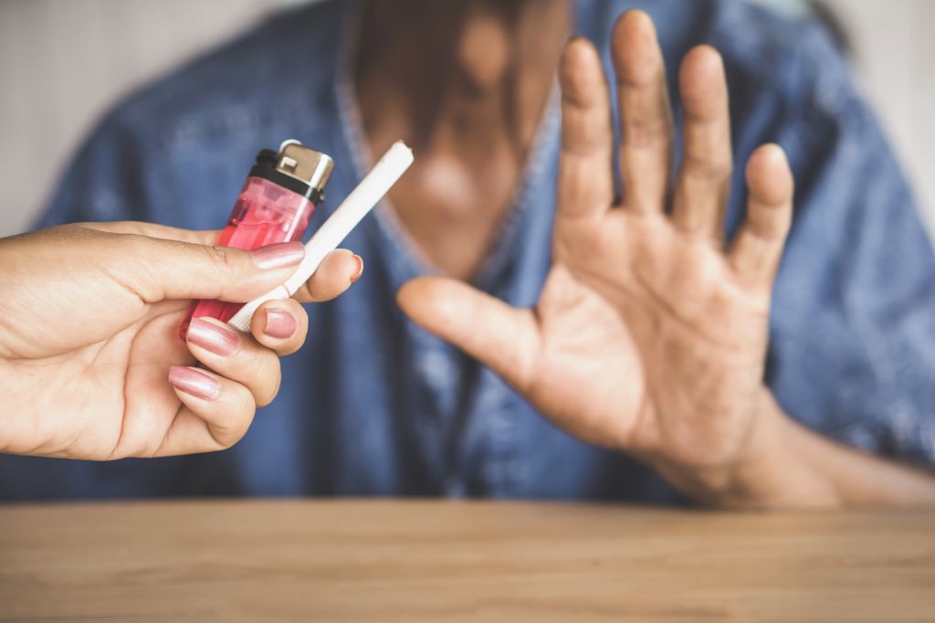 hand held up, not accepting the cigarette and lighter being offered by another person's hand