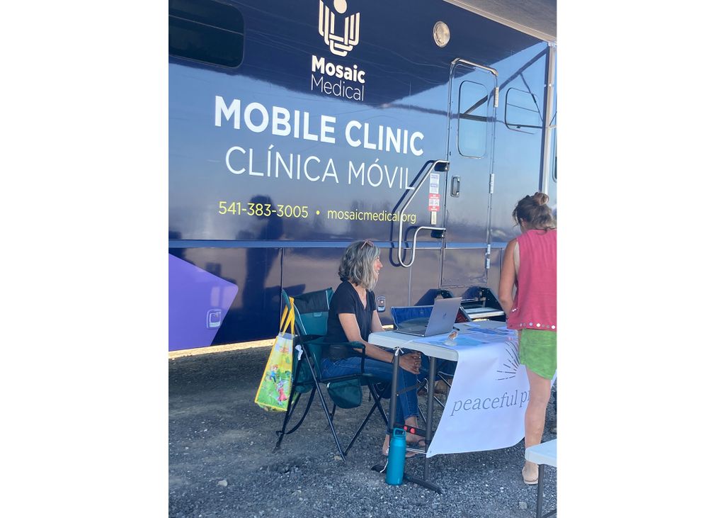 death doula Elizabeth Johnson sits in a chair in front of a vehicle marked 'mobile clinic'