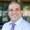Nizar Chahin, M.D., tiene el pelo negro corto y viste una camisa de vestir blanca y corbata, de pie en un patio del edificio 1 del Centro de Salud y Curación de OHSU.