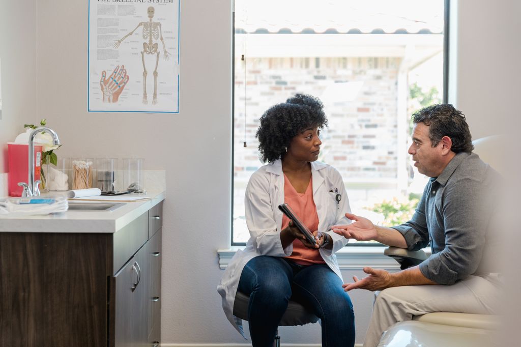 Female doctor and male patient in exam room discussing health information.