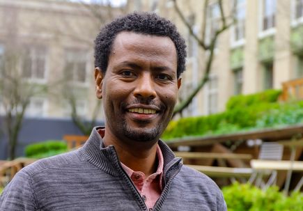 Fikadu Tafesse, Ph.D. (OHSU) a tall man with dark hair, smiling outside the Vollum garden at OHSU.