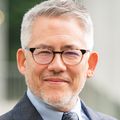 Aaron Caughey, M.D., Ph.D., has short gray hair, a gray suit, eye glasses, facial hair, and smiling.