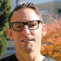 Craig Newgard, M.D., M.P.H., Tiene cabello castaño claro corto, anteojos negros y usa una chaqueta de OHSU, sonriendo en el césped de OHSU con el edificio del Hospital OHSU detrás de él.