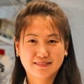 Haijiao Zhang, que está sonriendo, tiene el pelo oscuro recogido hacia atrás y viste una chaqueta azul con una camiseta roja, blanca y azul.