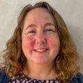 Anne King, M.B.A., tiene el pelo rizado hasta los hombros y sonríe.