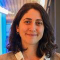 Ece Eksi, Ph.D., tiene el cabello oscuro y ondulado hasta los hombros y sonríe cerca del jumbo tron ​​de Knight Cancer en el Knight Cancer Institute.