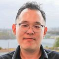 El joven Hwan Chang, Ph.D., tiene cabello oscuro, corto y ondulado, gafas y una camisa negra, y está sentado en su escritorio con una pantalla de computadora que muestra datos.