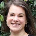 Rebecca Jungbauer, Dr.PH., M.A., has shoulder-length brown hair and a blue top, smiling in a garden area near Doernbecher Children's Hospital.