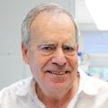 Eliot Spindel, M.D., Ph.D., tiene el pelo corto y blanco, una camisa de vestir blanca y sonríe en su laboratorio.