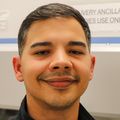 Christian Huertas Pagan has short black hair, light facial hair, an OHSU jacket, and smiling next to a hood in the Maternal Medicine Lab.