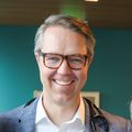 Eric Roeland tiene el pelo corto y claro y gafas, y sonríe.