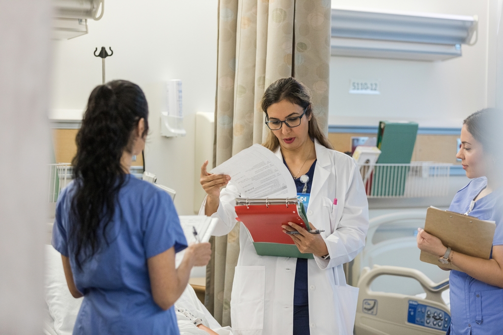 Three people in hospital gowns in health care training learning setting.