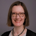 Deanne Tibbitts tiene el pelo oscuro hasta los hombros y gafas, y sonríe.