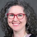Sarah Lowry, D.N.P. (OHSU) tiene el pelo oscuro hasta los hombros y gafas, y sonríe.