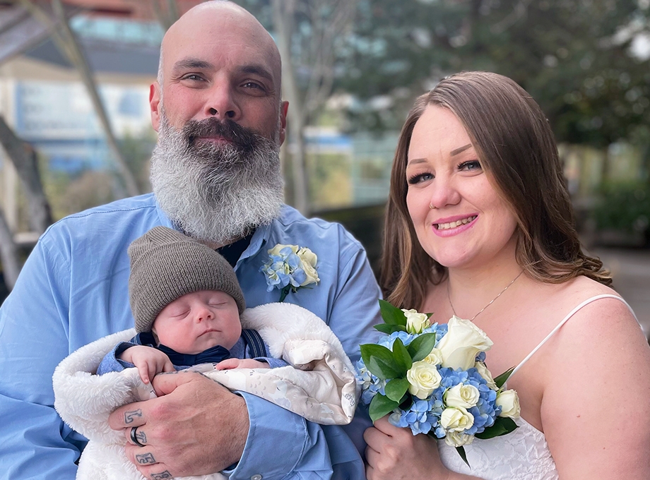 La familia Biritz sonriendo en el jardín de rosas de OHSU. Jessica y Marc Biritz, de Grants Pass, Oregón, habían estado en Doernbecher desde que su hijo, Malakai, nació con gastrosquisis, una anomalía de nacimiento de la pared abdominal que puede hacer que algunos órganos se encuentren fuera del cuerpo del bebé. Las tensiones y las cargas financieras estaban aumentando. Una asociación colaborativa entre profesionales legales y médicos de OHSU ayuda a los pacientes a resolver los factores sociales, económicos y ambientales que contribuyen a las desigualdades en salud. (Cortesía de la familia Biritz)