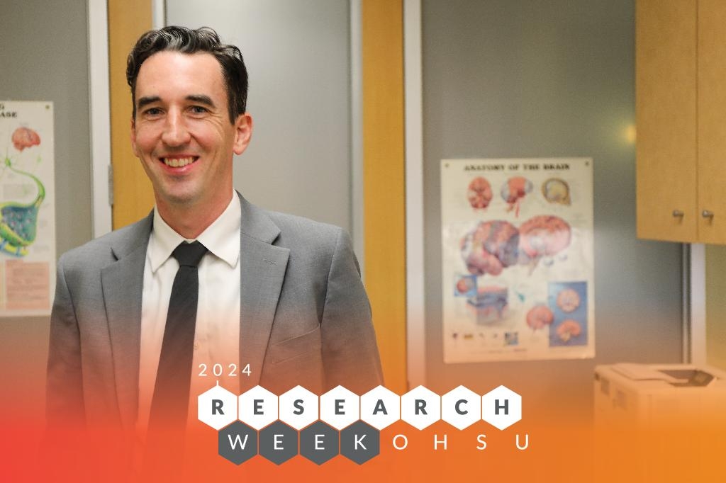 Dan Cleary - Research Week 2024. Cleary is tall with dark short hair, smiling. Wearing a gray suit and black tie, standing in an office at the OHSU Center for Health and Healing.