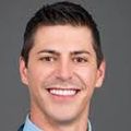 Adam Crosland, M.D., M.P.H. (OHSU) tiene cabello castaño corto y viste un traje y corbata azul/gris, sonriendo sobre un fondo gris oscuro.