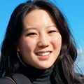 Lori Sun tiene el pelo largo y oscuro y lleva un abrigo en un entorno soleado de playa.