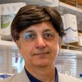 Sanjay Malhotra, Ph.D., con cabello corto y oscuro, anteojos y bata blanca, está de pie en su laboratorio de investigación del cáncer.