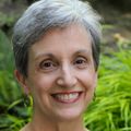 Sue Aicher, Ph.D., tiene el pelo corto y gris, una blusa azul y sonríe en un jardín cerca del Casey Eye Institute.
