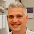 Jonah Sacha, Ph.D., con una camisa blanca y cabello gris, sonríe en su laboratorio.