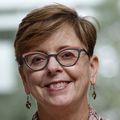 Nancy Haigwood, Ph.D. Tiene cabello castaño rojizo corto y un suéter rosa, de pie con los brazos cruzados en lo alto de las escaleras con una gran ventana detrás de ella que muestra árboles.