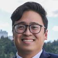 Huan Vo, M.D., has short dark hair, a dark suit and blue shirt, eyeglasses, and standing on a balcony of CHH1 at OHSU.