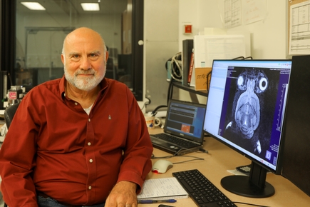 Martin Pike has a red shirt, very short gray hair, smiling in front of computer images at AIRC. Martin Pike, Ph.D., pictured with image of a mouse brain taken at the AIRC. (OHSU/Christine Torres Hicks)