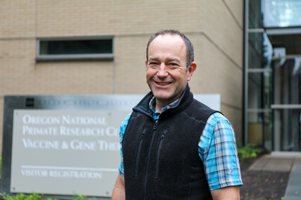 Matthias Schabel, Ph.D., has a black vest and aqua shirt, standing at the Vaccine and Gene Therapy Institute building. (OHSU/Christine Torres Hicks)