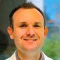 Lee Neilson, M.D., tiene el pelo corto de color castaño claro, una bata blanca y sonríe cerca de su oficina en OHSU.