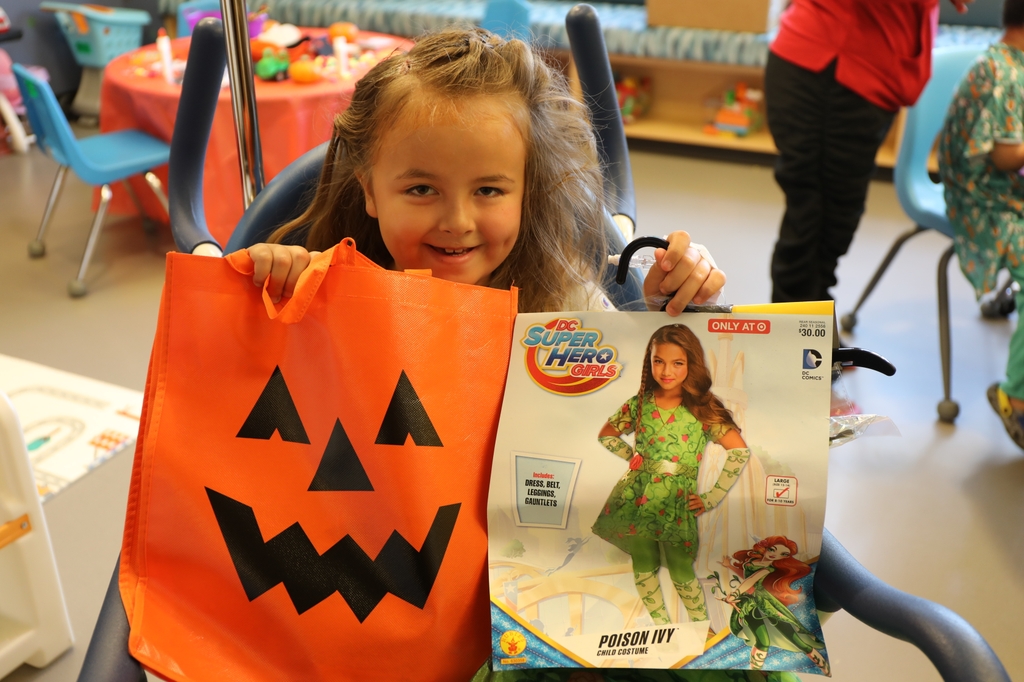 young girl holding orange jack-o-lantern treat bag and package with child's poison ivy character costume
