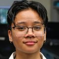 Ellala Limoico has short dark hair, eye glasses and wearing a white coat while standing in the lab at OHSU.