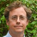Eran Klein, M.D., Ph.D., wears a light blue patterned dress shirt and glasses, has light brown curly hair, smiling in a garden area of the VA Hospital. (OHSU/Christine Torres Hicks)