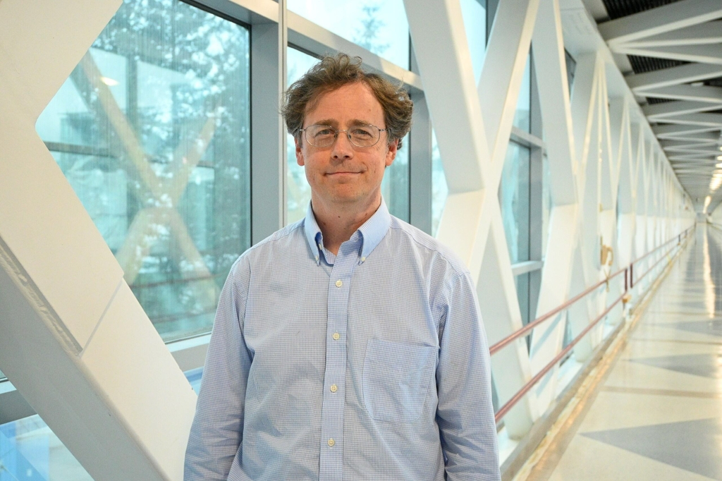 Eran Klein, M.D., Ph.D., wears a light blue patterned dress shirt and glasses, has light brown curly hair, smiling on the VA/OHSU bridge at OHSU. New portable MRI technology has the potential to enhance research and clinical care in underserved areas, but must be developed with careful attention to ethical, privacy, and safety concerns, according to study lead author Eran Klein, M.D., Ph.D. (OHSU/Christine Torres Hicks)