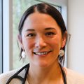 Emily Yang, M.D., tiene el cabello largo y oscuro recogido en una cola de caballo baja y está sonriendo en el vestíbulo del Hospital Infantil Doernbecher.