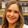 Lauren Rust, Ph.D., tiene el pelo largo y suelto y rizado, con raya a un lado, una camiseta blanca sin mangas y sonríe en el laboratorio.