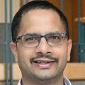 Saurabh Thosar, Ph.D., tiene cabello negro corto, bigote, gafas, viste una bata blanca y está sonriendo en una sala de estudio del sueño.