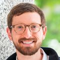 Kevin Guttenplan, Ph.D. has short red hair, eye glasses and a black top, standing near the Vollum Institute.