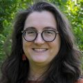 Jennifer Jahncke, Ph.D., tiene cabello largo y ondulado de color castaño, un suéter naranja y anteojos, parada en el césped con OHSU detrás de ella.