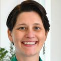 Renee Ryals, Ph.D., tiene el pelo corto y oscuro, una chaqueta verde y una blusa negra, y sonríe en el Casey Eye Institute.