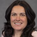 Summer Gibbs, Ph.D., tiene el pelo largo y ondulado, un suéter rosa claro y sonríe sobre un fondo gris.