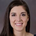 Jennifer Fowler, Au.D., has long straight brown hair, a dark blue top and smiling against a brown background.