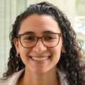 Devlynne Sasha Ondusko, M.D., tiene cabello largo y oscuro y rizado, anteojos y bata blanca, y sonríe en el pasillo cerca de la UCIN de OHSU. 